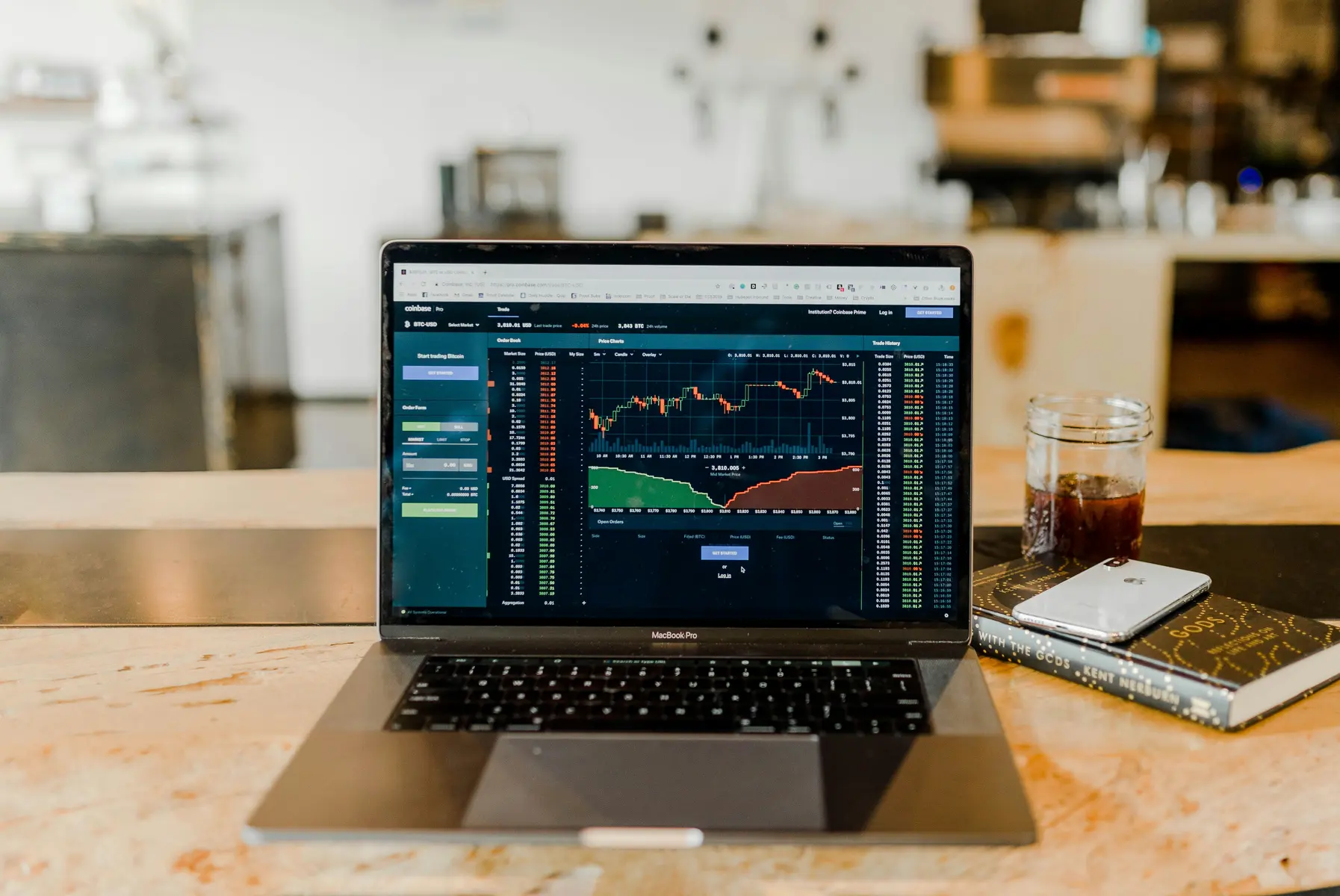 Ein Laptop auf einem Holztisch zeigt Trading-Charts und ein Orderbuch für Finanzmärkte.