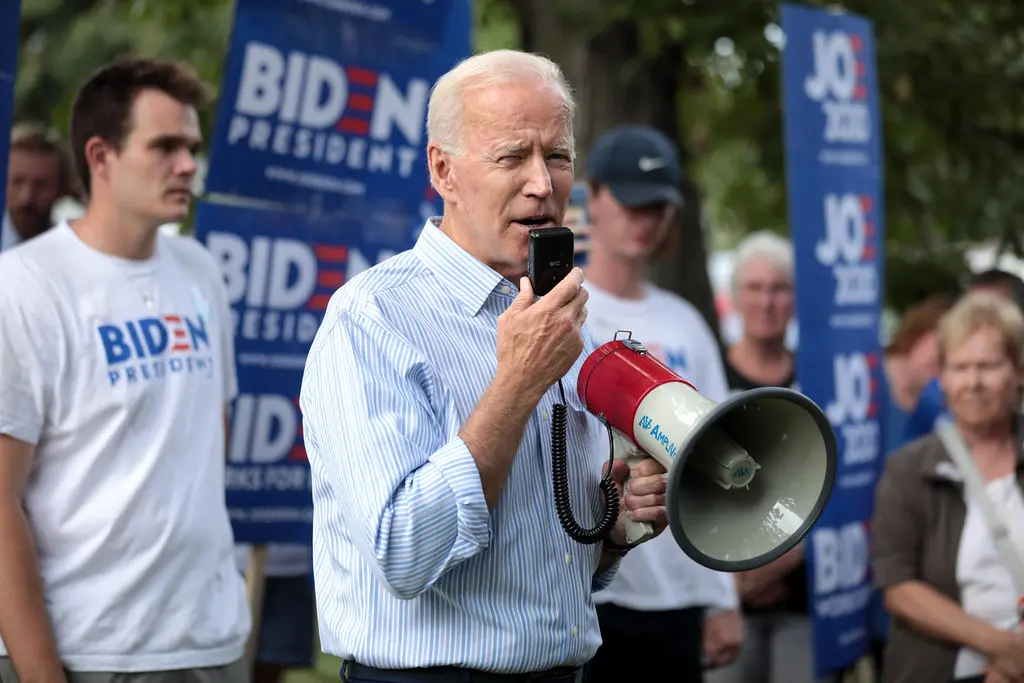 Joe Biden spricht mit einem Megafon vor einem Hintergrund mit Wahlplakaten.