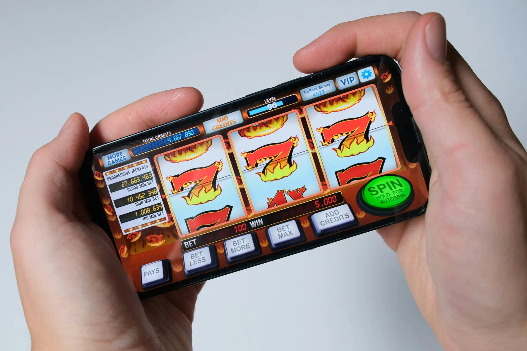 Eine Person hält ein Smartphone mit einem digitalen Slot-Maschinenspiel auf dem Bildschirm.