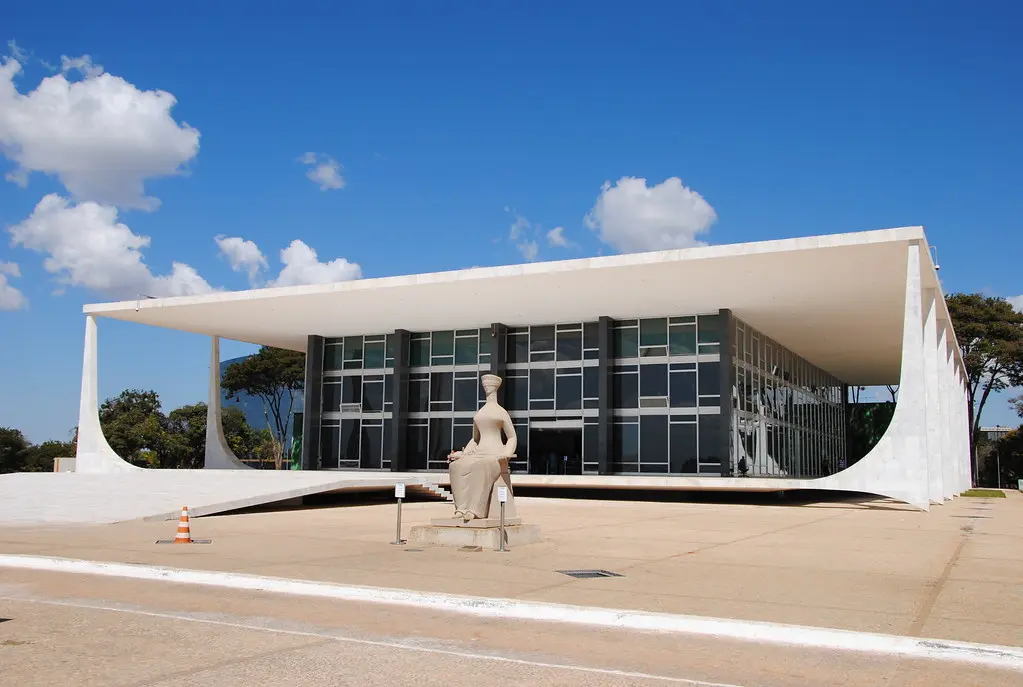 Das Gebäude des Supremo Tribunal Federal in Brasília mit einer Statue im Vordergrund unter blauem Himmel.