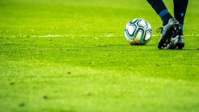 Voetbal en benen van een voetballer op een grasmat.