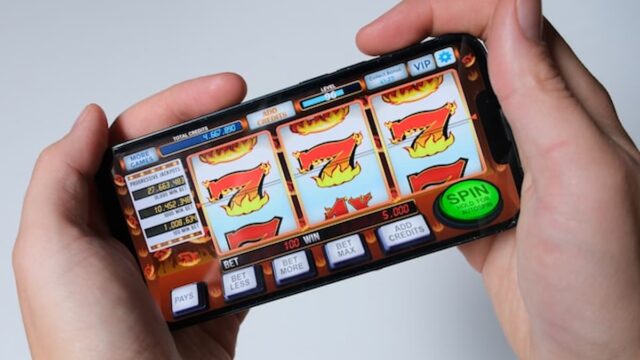 A person holding a smartphone displaying a slot-style casino game interface.