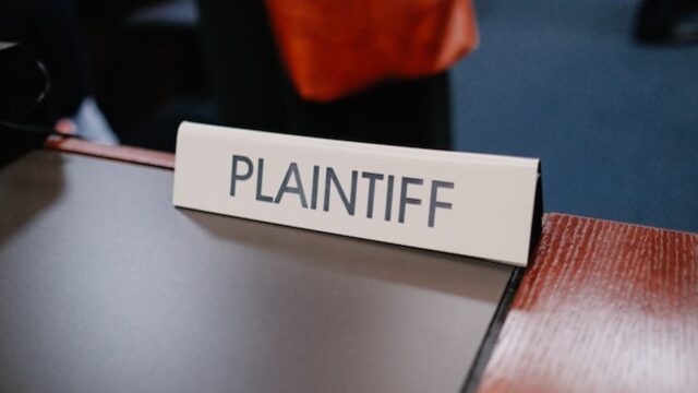 A courtroom scene showing a “Plaintiff” nameplate