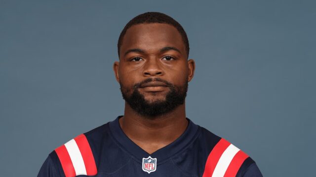 A professional football player wearing a dark blue jersey standing against a blue studio background