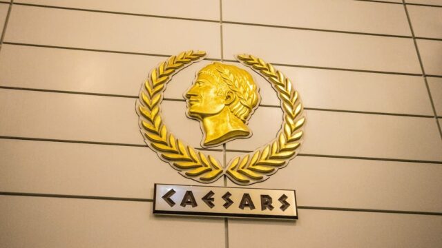 Gold Caesars profile logo with laurel wreath mounted above Caesars signage on a beige exterior wall