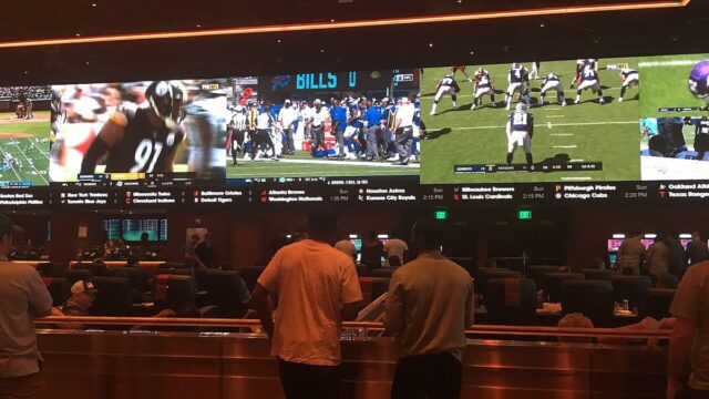 Patrons standing at a casino sportsbook counter watching multiple football games on large video screens