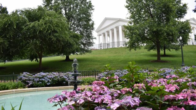 Virginia State Capitol building in Richmond, with white columns on a hill overlooking a fountain and pink flowers in the foreground