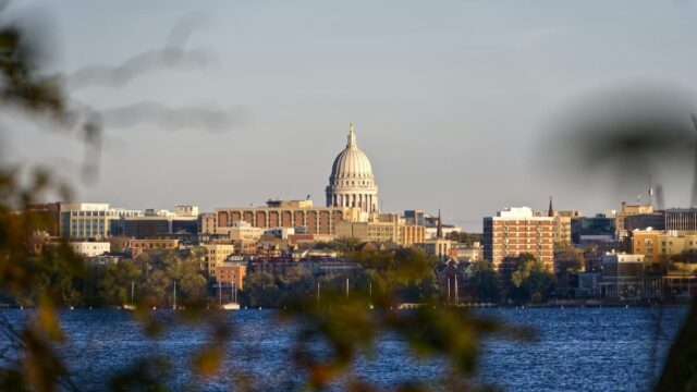 Wisconsin State Capitol dome and downtown Madison skyline viewed across Lake Monona with trees in the foreground