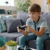 Boy playing video games on a controller while sitting on a couch at home