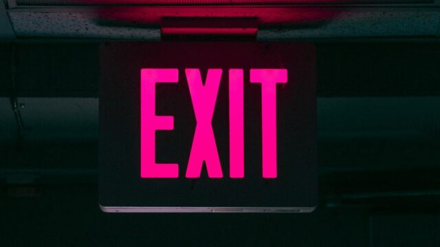 Neon pink doorway exit sign shines against dark background