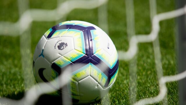 Soccer ball on grass seen through a goal net on a football pitch
