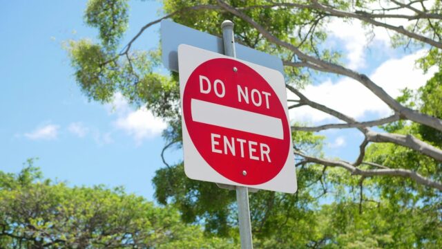 Red and white Do Not Enter road sign with trees and blue sky in the background