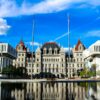 New York State Capitol building in Albany reflected in a pool under a blue sky