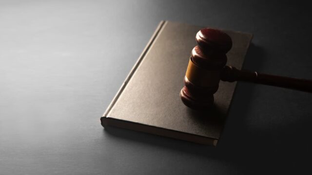 A judge’s gavel resting on a law book on a dark surface.