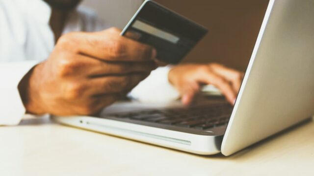 A person holding a payment card while using a laptop computer.