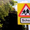 Close up of a yellow school zone sign against a background of sky and tree canopy