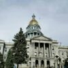 Colorado State Capitol building in Denver with its gold-domed roof visible above the main entrance and surrounding trees.