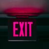 Illuminated red EXIT sign mounted on a ceiling in a dark building corridor