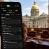 Smartphone displaying live micro-betting markets with the New Jersey State House visible in the background.