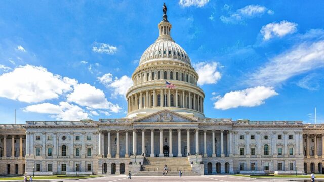 Front view of the United States Capitol building beneath a blue sky with scattered white clouds.