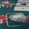 A poker player reveals a pair of aces next to poker chips on a gaming table.