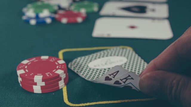 A poker player reveals a pair of aces next to poker chips on a gaming table.