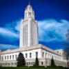 Exterior view of the Nebraska State Capitol building in Lincoln under a blue sky with white clouds.