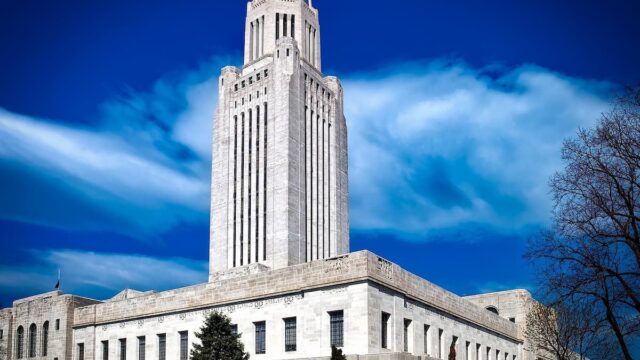 Exterior view of the Nebraska State Capitol building in Lincoln under a blue sky with white clouds.