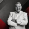 Black-and-white portrait of SafeBets CEO Alex Konanykhin with red geometric background elements