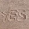 A checkmark and the word “YES” drawn in sand, representing shareholder approval.