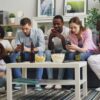 Group of friends using smartphones while watching sports together at home