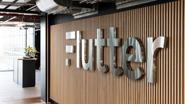 Flutter Entertainment logo mounted on a wooden wall inside a company office.