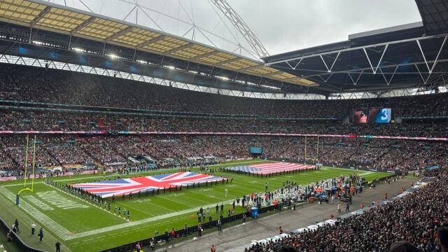 Packed Wembley Stadium with U.K. and U.S. flags displayed across the field before an NFL game.