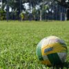 Brazil-themed soccer ball resting on a grassy soccer field with a goal and player in the background.