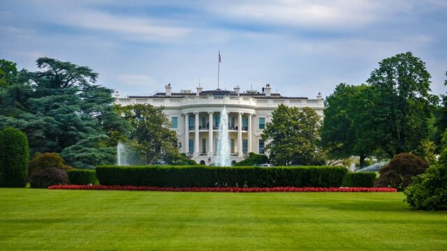 The White House seen from the South Lawn in Washington, D.C., with trees, fountains and landscaped grounds in the foreground.